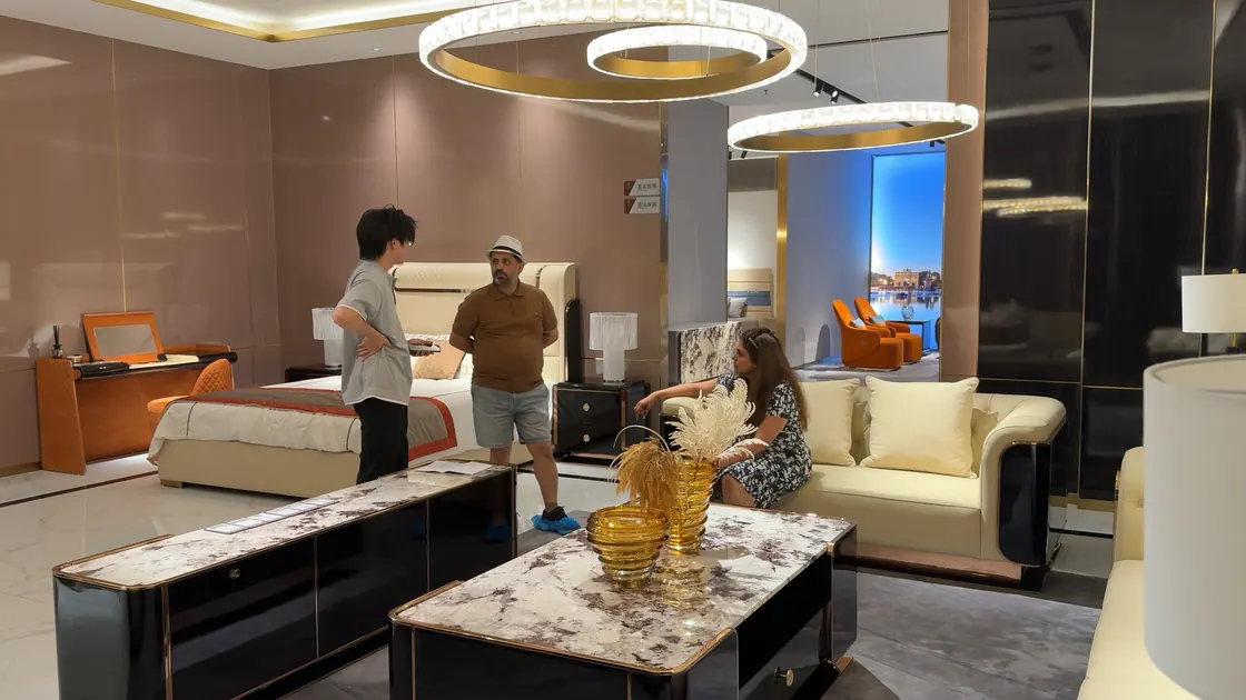 Three people talk beside a sofa and patterned low tables in a showroom.