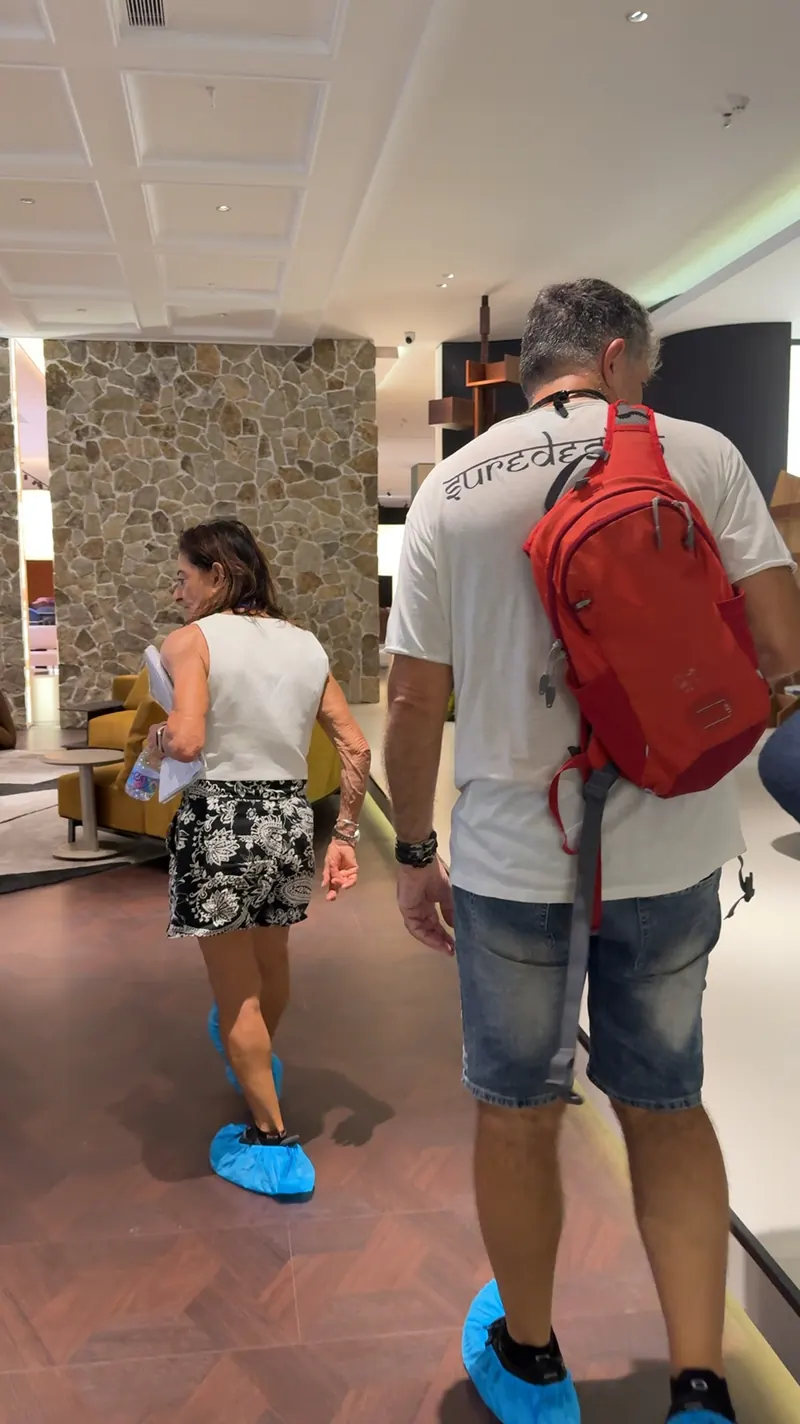 Two adults walk through furniture displays while carrying papers.